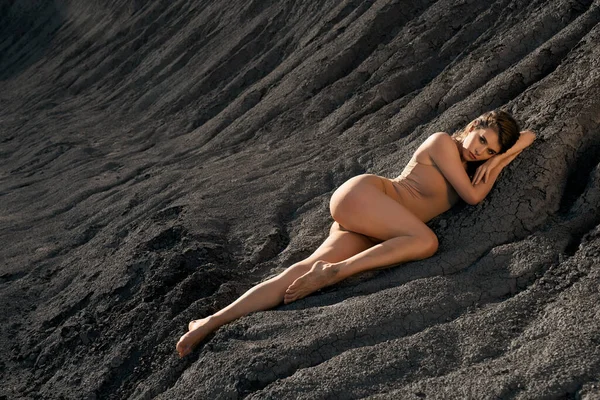 Mulher deslumbrante deitada em solo preto seco na pedreira. — Fotografia de Stock