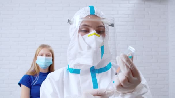 Медсестра в антивирусном костюме набирает лекарства в шприц для девушки с инъекцией. — стоковое видео