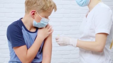 Korumalı maskeli hemşire çocuk için koronavirüsten iğne yapıyor..
