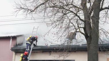 Kasklı itfaiyeciler çatıda hortumla yangını söndürüyor..