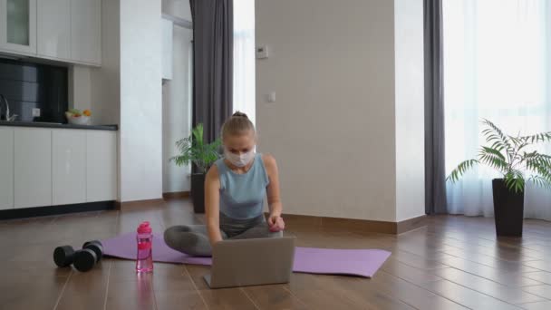 Mulher em máscara usando laptop para treino doméstico — Vídeo de Stock