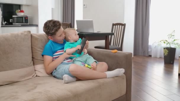 Dospívající chlapec sedí na gauči s mladším bratrem — Stock video