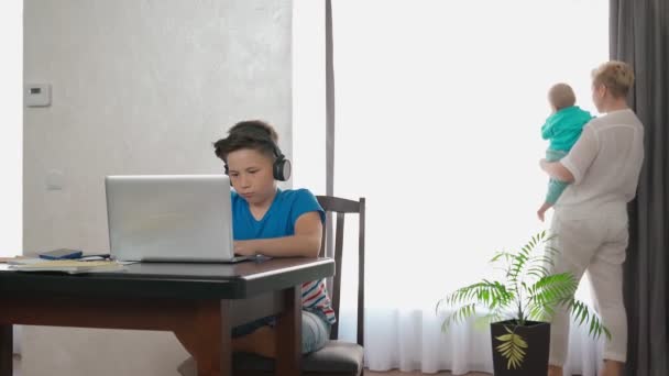 Chlapec hraje na notebooku, zatímco matka nese batole — Stock video