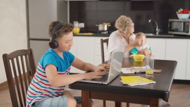 Chlapec hraje na notebooku, zatímco žena krmení dítě — Stock video