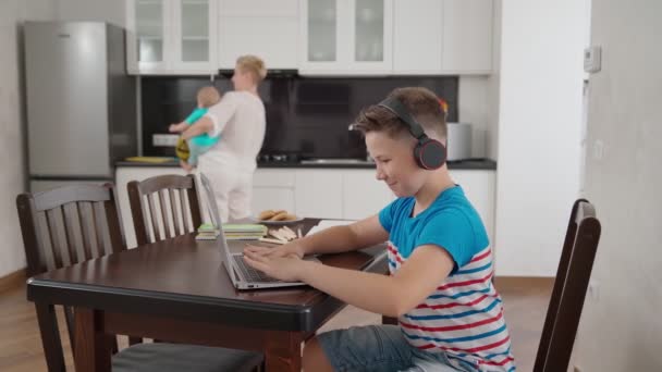 Teenager benutzt Laptop, während Mutter Hausarbeiten erledigt — Stockvideo
