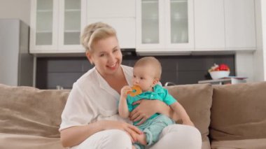 Gülümseyen kadın bebeğini kucağında tutuyor ve video görüşmesi yapıyor.