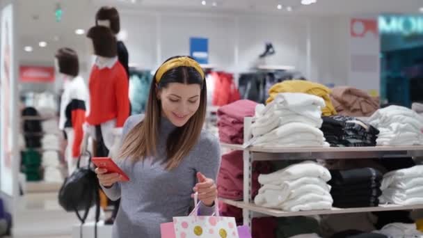 Mujer embarazada con bolsas de compras usando teléfono inteligente — Vídeo de stock