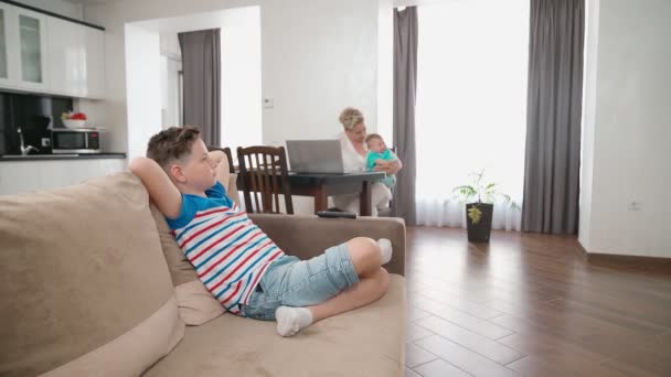 Roztomilý chlapec relaxaci na gauči, zatímco matka hraje s batole — Stock video