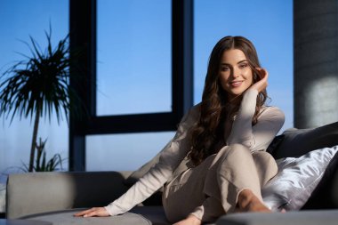 Çekici kadın kanepede dinlenirken kamerada gülümsüyor.