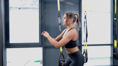 Genç sportif kadın TRX 'te çömeliyor..