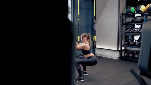 Mujer joven en cuclillas con sistema trx en el gimnasio moderno. — Vídeo de stock