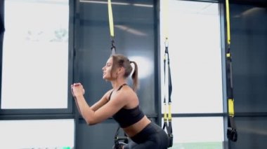 Sportif kadın trx sisteminde çömeliyor..