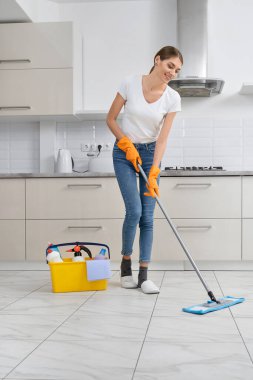 Mutfakta yerleri yıkayan gülümseyen genç kadın..