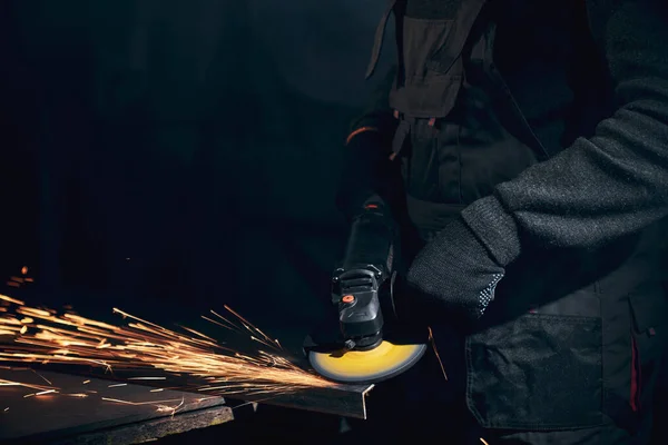 Worker in black gloves working angle grinder with metal.