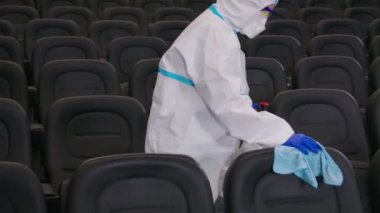 Koruyucu üniformalı bir adam sinemaya dezenfektan sıkıyor.
