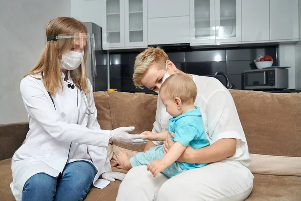 Pediatra en máscara protectora revisando bebé en casa — Foto de Stock