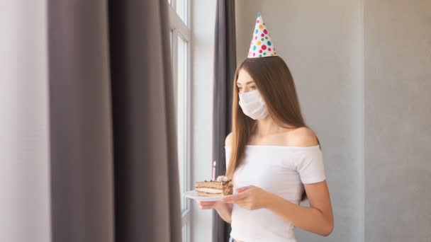 Jovem mulher vestindo máscara facial transportando bolo perto da janela. — Vídeo de Stock