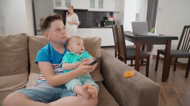 Два мальчика смотрят телевизор, пока мама разговаривает по мобильному — стоковое видео