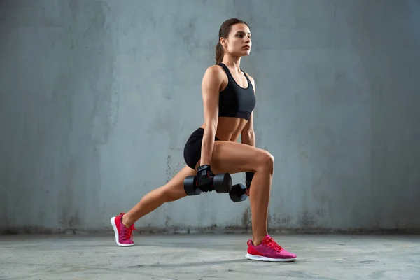 Deportiva haciendo embestidas usando mancuernas. — Foto de Stock