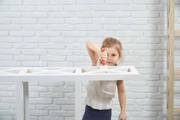 Симпатична маленька дівчинка малює дерев'яну стійку в білому кольорі . — стокове фото