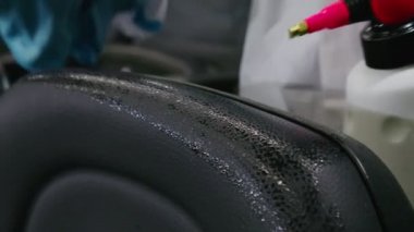 Koruyucu beyaz elbiseli bir adam sinemada sandalyeyi dezenfekte ediyor.