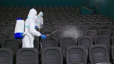 Koruyucu kıyafetli adamlar sinema salonunda dezenfektan sıkarlar.