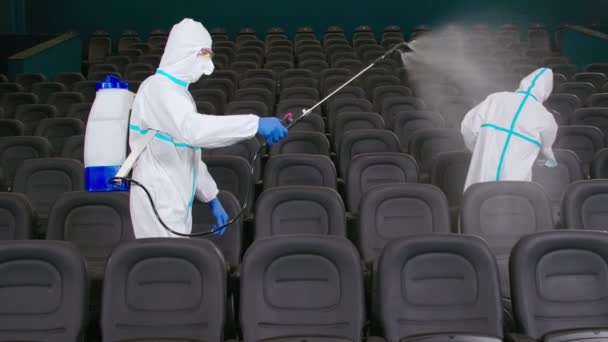 Двое мужчин чистят кинотеатр, распыляя дезинфицирующее средство — стоковое видео