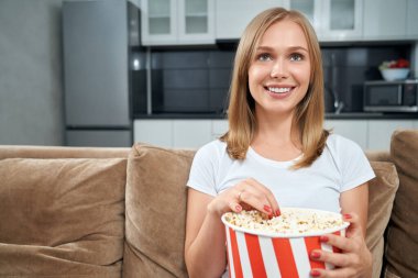 Genç bir kadın film izliyor ve evde patlamış mısır yiyor.