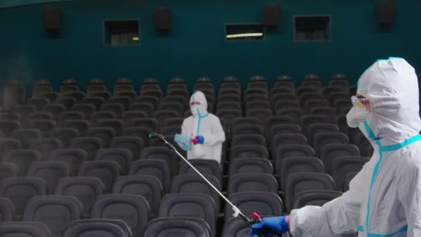 Deux hommes en uniforme de protection faisant la désinfection du cinéma — Video