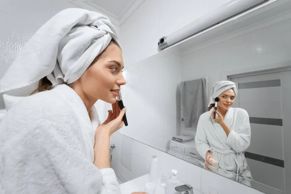 Feliz joven confiada con toalla en la cabeza haciendo maquillaje. —  Fotos de Stock