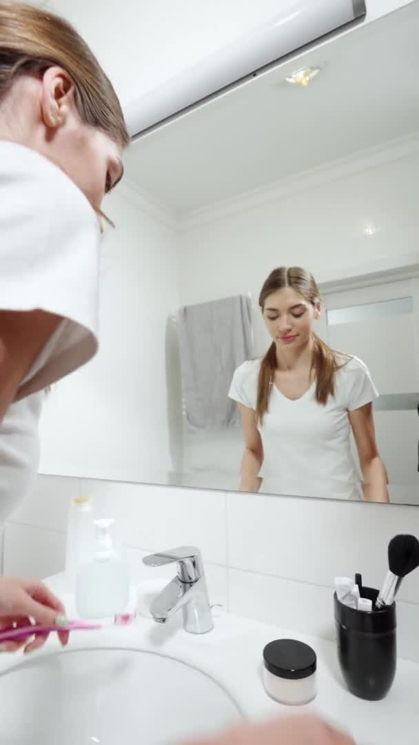 Jeune femme debout regardant miroir et brossant les dents. — Video