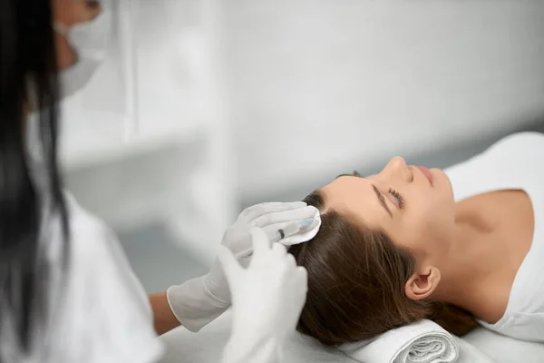 Schoonheidsspecialiste in beschermend masker doet procedure voor het haar. — Stockfoto