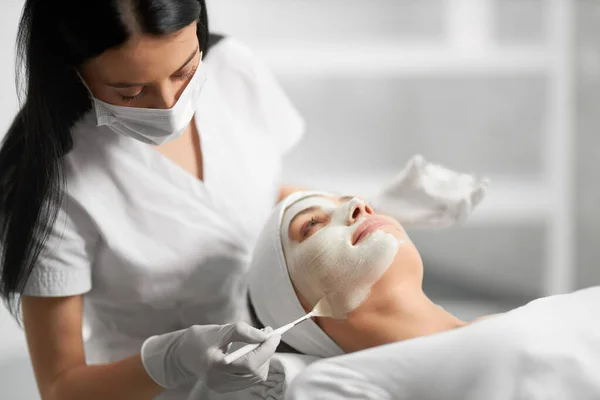 Esteticista aplicando crema blanca especial para el paciente. — Foto de Stock