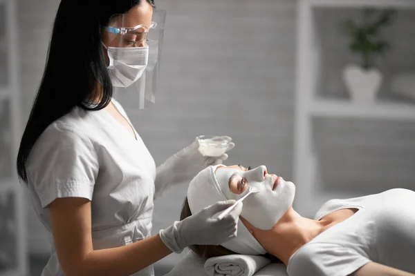Esteticista haciendo limpieza de cara con cosméticos para el paciente. — Foto de Stock
