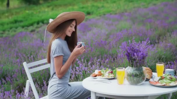 Улыбающаяся девушка пьет кофе на лавандовом поле. — стоковое видео