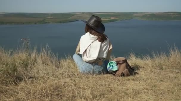 Jonge vrouw in cowboy hoed zitten op rand van de berg — Stockvideo