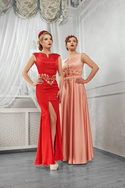 Två unga, vackra kvinnor i lång, kväll röd och persika klänning — Stockfoto