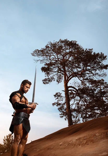 Junger muskulöser Krieger mit Schwert in den Bergen — Stockfoto