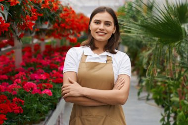 Önlüklü güzel bir kadın çiçeklerin arasında poz veriyor.