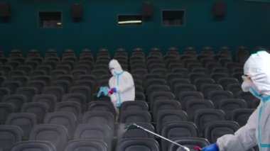 Koruyucu kıyafetli iki adam sinemayı dezenfekte ediyor.