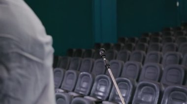 Koruyucu kıyafetli bir adam sinemaya dezenfektan sıkıyor.