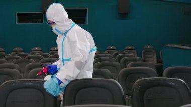 Anti-virüs üniformalı bir adam sinemaya dezenfektan sıkıyor.