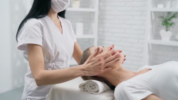 Esteticista haciendo masaje facial para mujer joven. — Vídeo de stock