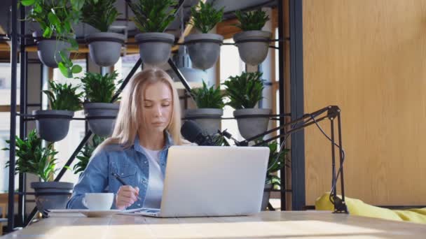 女性博主坐在咖啡店，手持笔记本电脑和话筒 — 图库视频影像