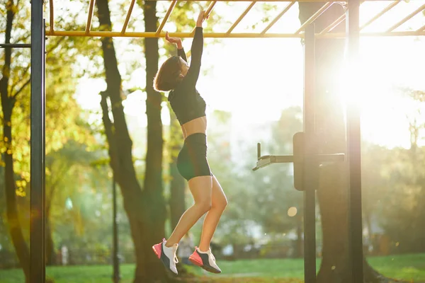 Женщина висит на горизонтальной панели во время тренировки на открытом воздухе — стоковое фото