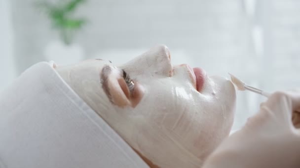 Estetista applicare speciale maschera bianca facciale per il cliente. — Video Stock