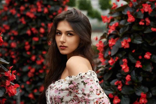 Kaunis nuori nainen poseeraa lähellä punaisia kukkia. — kuvapankkivalokuva