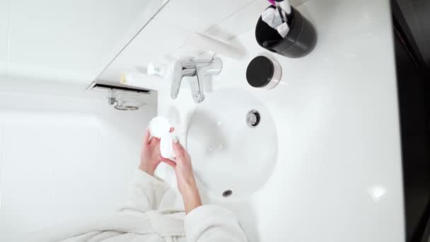 Souriant femme mignonne en utilisant la crème pour le visage dans la salle de bain. — Video