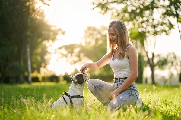Junge lächelnde Frau trainiert französische Bulldogge im Park. — Stockfoto