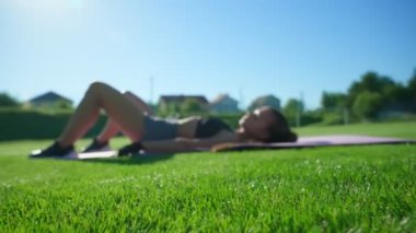 Woman practicing floor bridge butt raise exercises on grass.